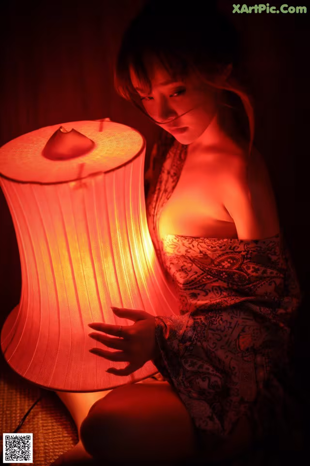 A woman in a kimono sitting next to a lamp.