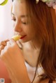 A woman with a flower crown on her head eating a piece of fruit.