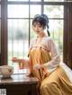 A woman in a yellow and white hanbok sitting on a table.