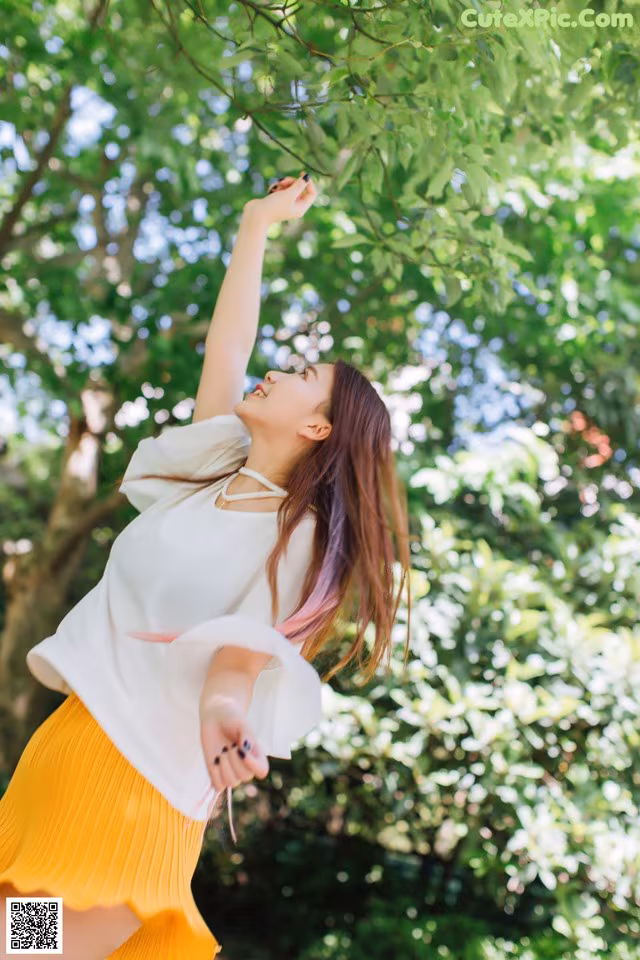 A woman in a white shirt and yellow skirt standing under a tree.
