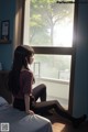 A woman sitting on a bed looking out a window.