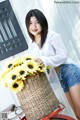 A woman standing next to a basket of sunflowers on a bike.