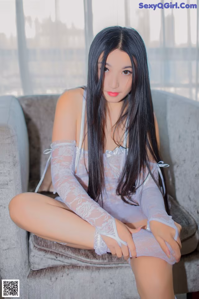 A woman sitting on a couch in a white dress.