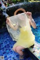 A woman in a yellow dress and straw hat sitting by a pool.