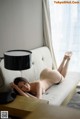 A naked woman laying on a couch next to a lamp.