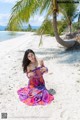 A woman in a colorful dress sitting on a sandy beach.