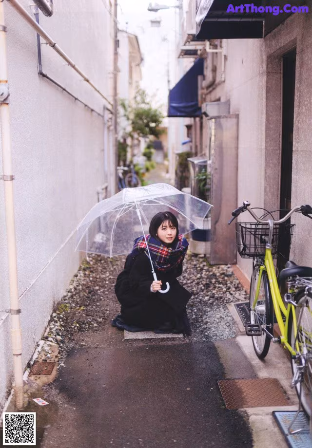A woman sitting on the ground holding an umbrella.