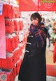 A woman standing in front of a store filled with red bags.