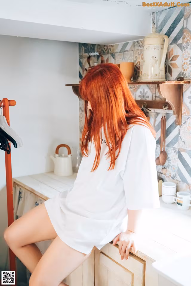 A woman with red hair sitting on a kitchen counter.