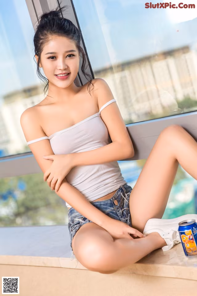 A woman sitting on a window sill next to a can of Pepsi.