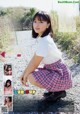 A young woman in a school uniform crouching down on a dirt road.