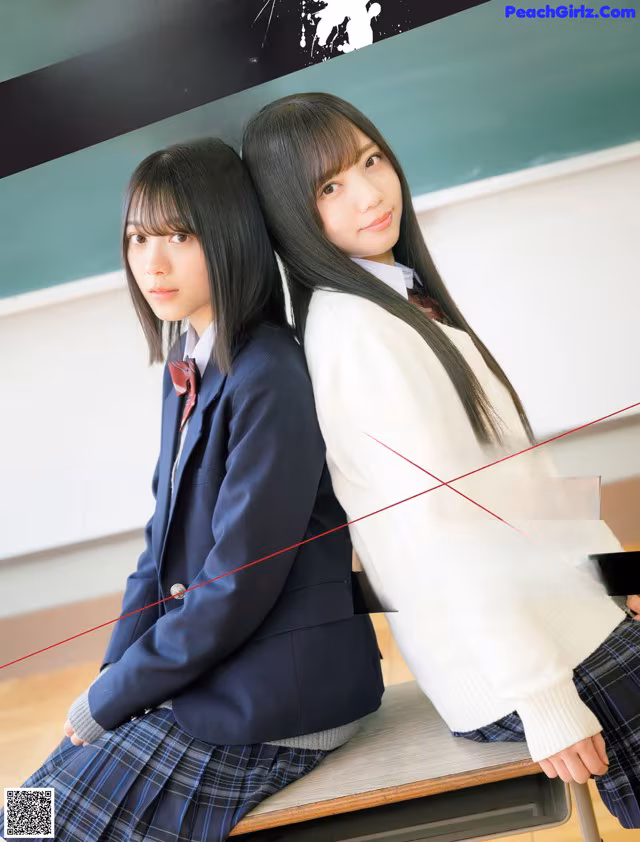 A couple of young women sitting on top of a desk.