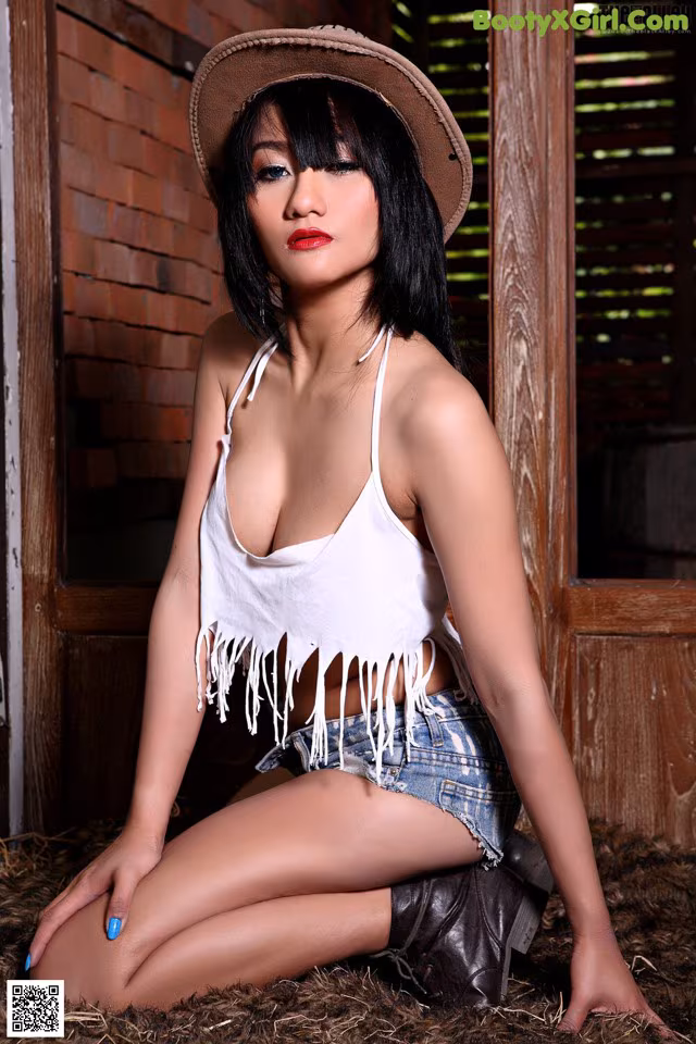 A woman in a cowboy hat sitting on a pile of hay.