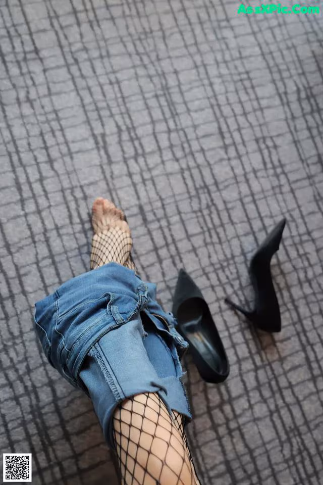 A woman wearing fishnet stockings and high heels laying on the floor.
