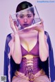 A woman in a purple corset holding a clear box over her face.