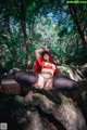 A woman in lingerie sitting on a rock in the woods.