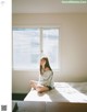 A woman sitting on a bed in front of a window.