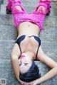 A woman in a pink top and black bikini laying on the ground.