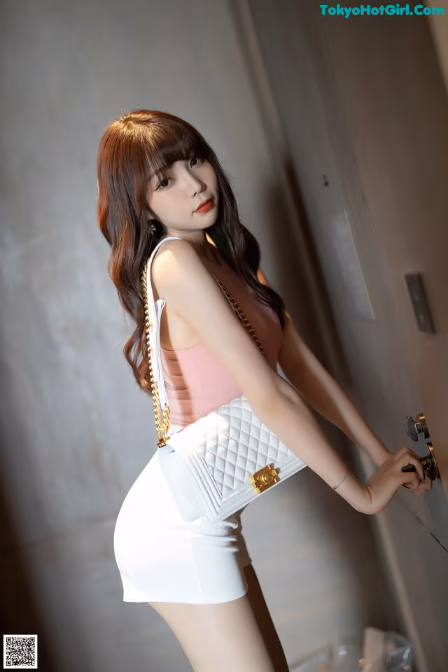 A woman in a pink top and white skirt holding a white purse.