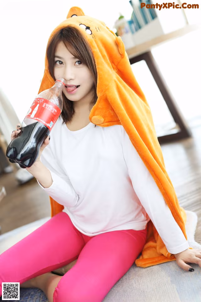 A woman sitting on the floor holding a bottle of soda.