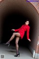 A woman in a red coat is posing in a tunnel.